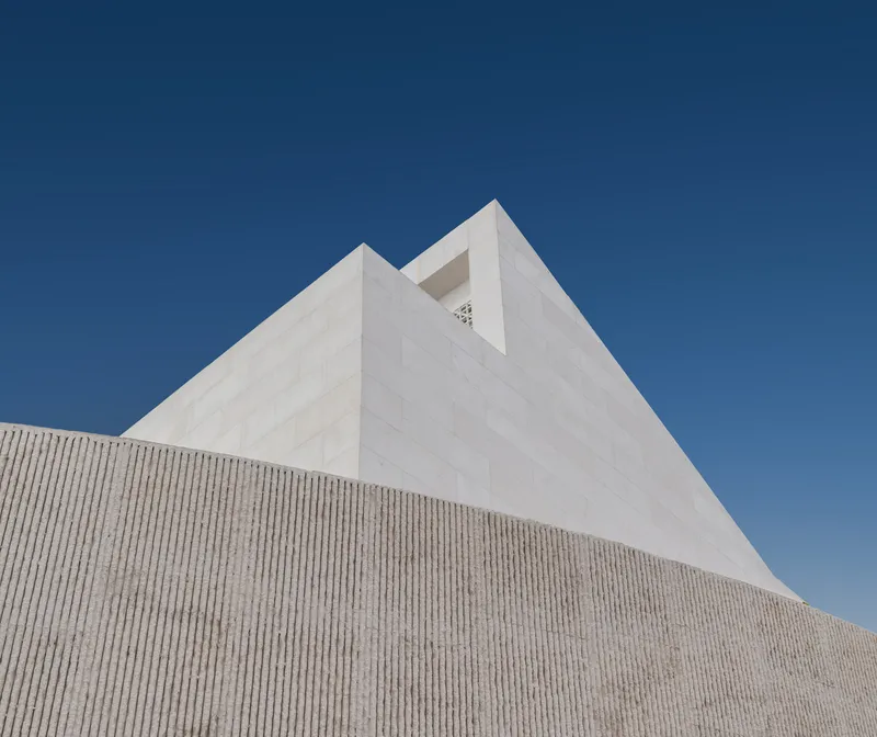 Upward view of the white rendered gable with notched profile above the textured concrete wall