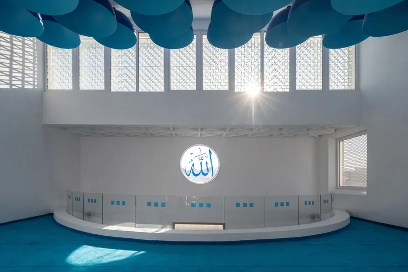 Curved raised platform beneath clerestory windows with patterned screens and teal acoustic ceiling discs overhead