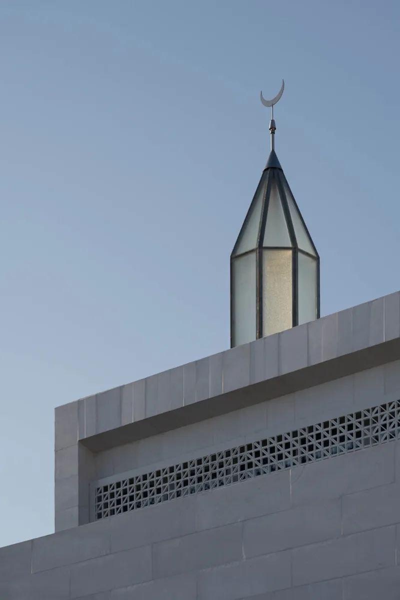 Glazed minaret tower topped with crescent finial rising above perforated screen parapet at twilight