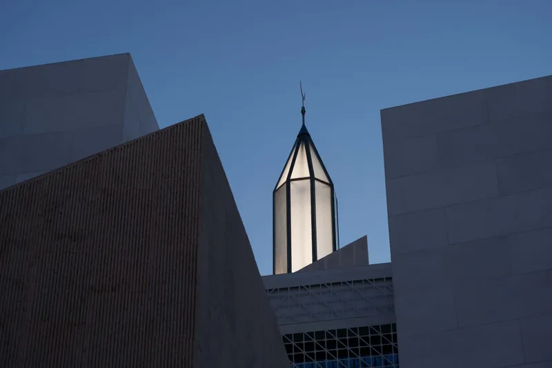 Upward view of a slender octagonal tower framed by the angular facades of surrounding volumes at dusk
