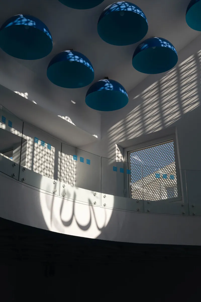 Interior prayer hall with teal dome pendants and light filtered through perforated screens creating shadow patterns