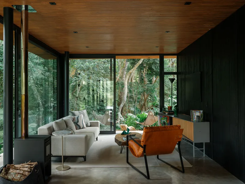Interior view through glass walls framing mature trees and layered forest canopy beyond