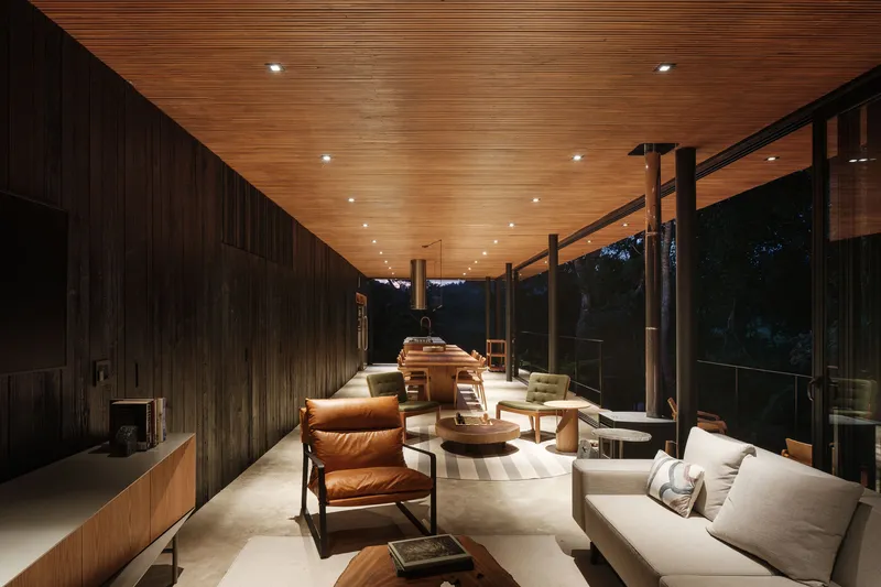 Living space illuminated at dusk with recessed ceiling lights and dark timber wall cladding