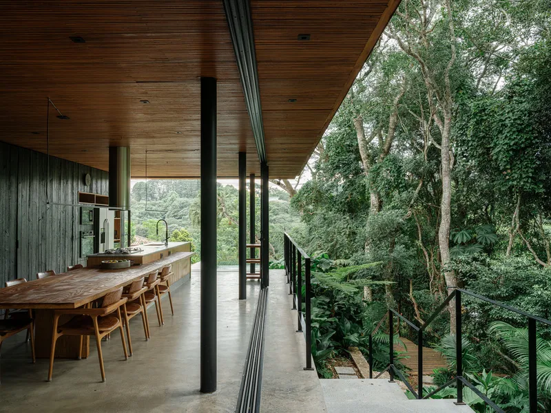 Open dining area with live-edge timber table and steel railing terrace facing a forested hillside