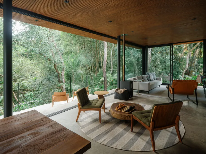 Living room with freestanding wood stove and floor-to-ceiling glass walls opening to surrounding forest