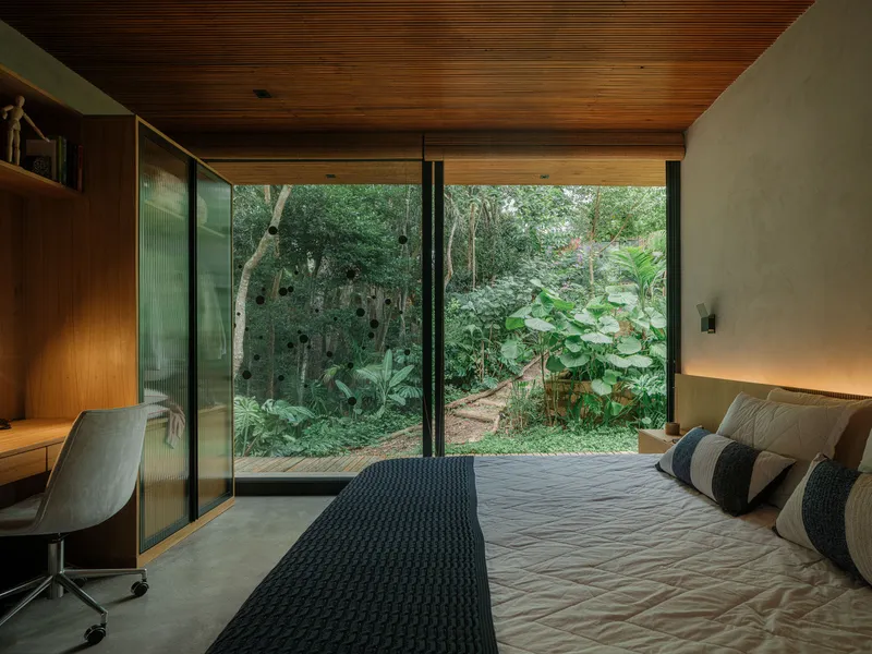 Bedroom with timber ceiling and floor-to-ceiling glazing opening onto a planted garden path