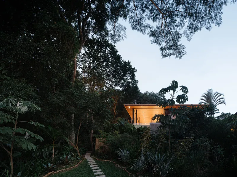 Distant view of the illuminated timber pavilion perched above landscaped garden beds at dusk