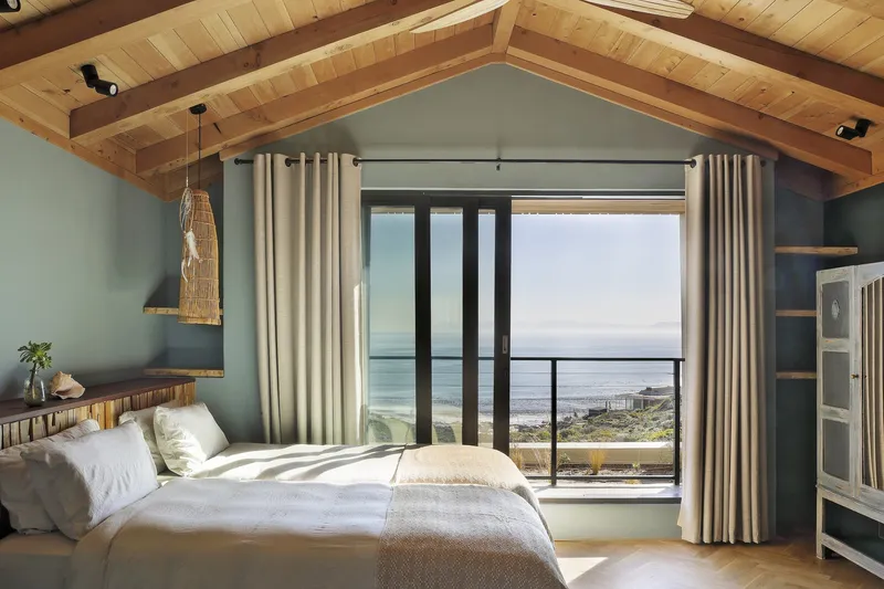 Bedroom with exposed timber ceiling rafters and sliding glass doors opening to an ocean view