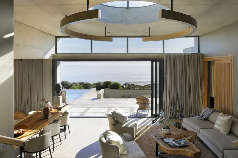 Double-height living room with circular oculus and floor-to-ceiling windows framing the ocean horizon