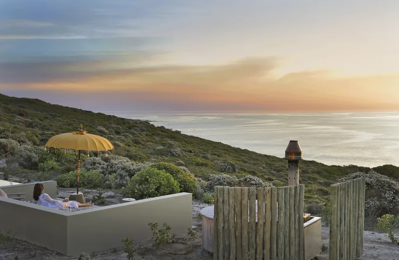 Rooftop terrace with yellow umbrella and timber windscreen fence on a coastal hillside at dusk