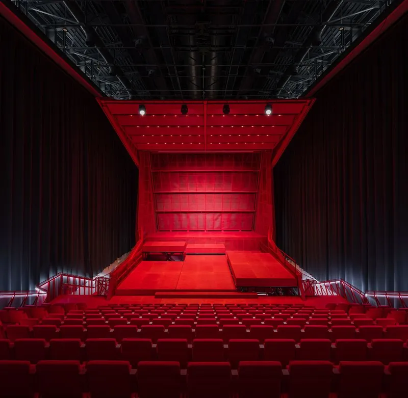 Looking up at the red illuminated stage canopy and exposed rigging infrastructure with black curtains flanking