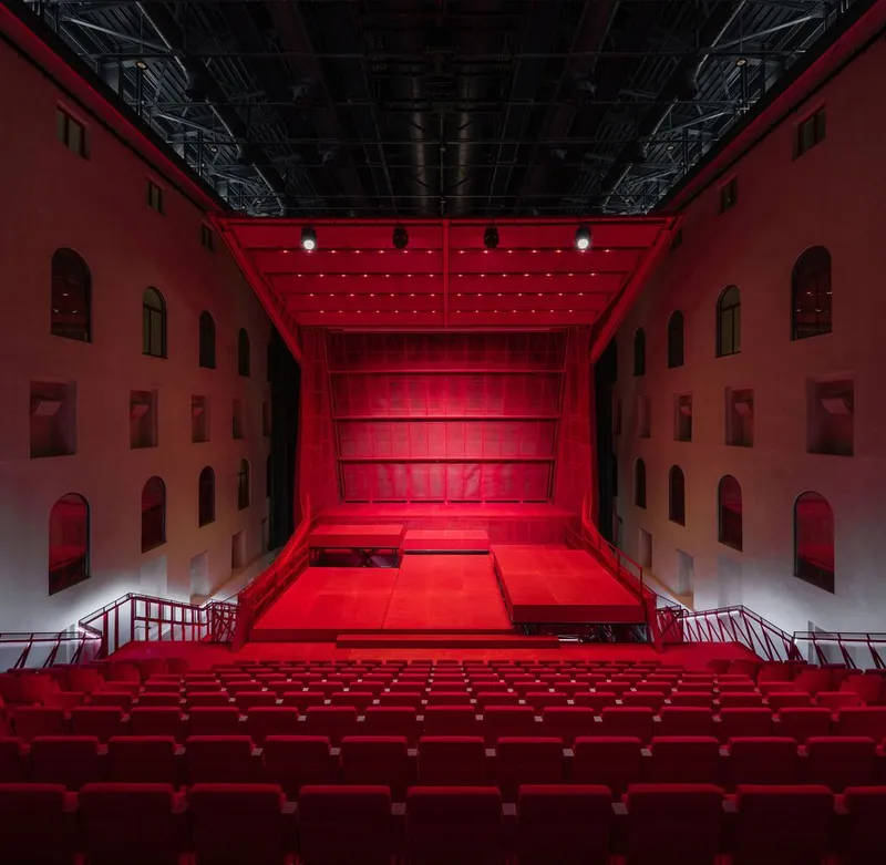 Auditorium view showing red seating tiers and stage platform beneath canopy surrounded by arched wall openings