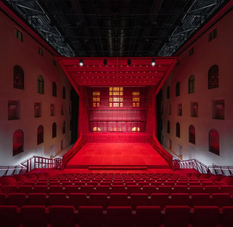 Central courtyard with red tiered seating facing multi-story arched openings illuminated by stage lights