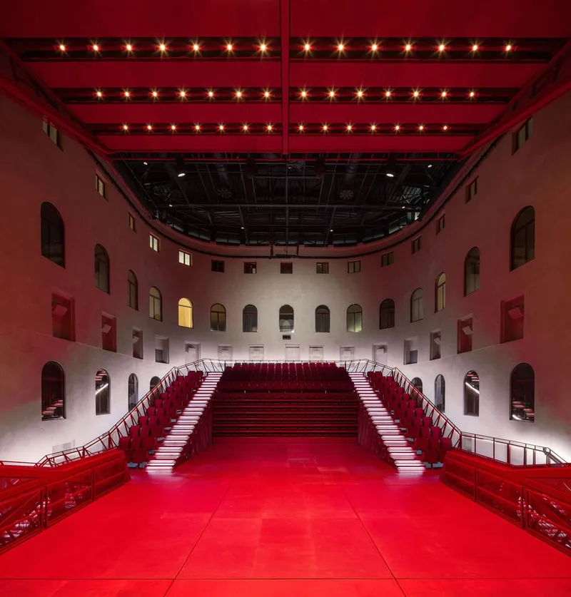 Symmetrical red staircase seating flanking a performance space beneath a suspended lighting grid