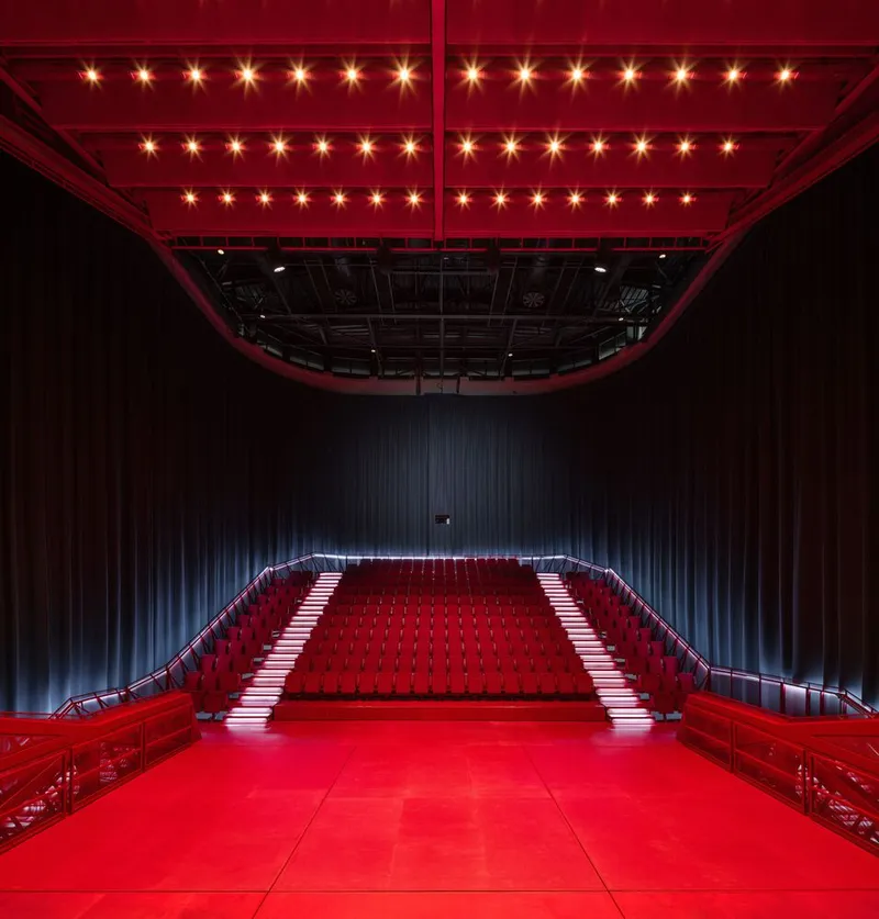Red carpeted performance platform with curved seating stairs under a canopy of overhead stage lights