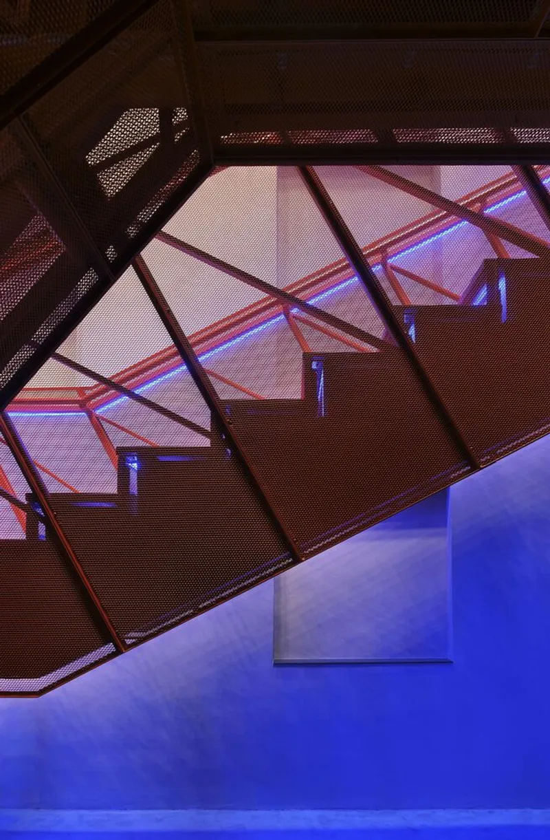 Upward view through perforated metal stair treads with angled steel bracing under purple light