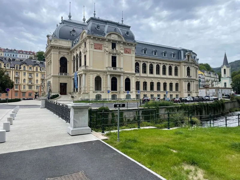 Beaux-Arts facade with mansard roof and arched entrance beside a river under cloudy skies