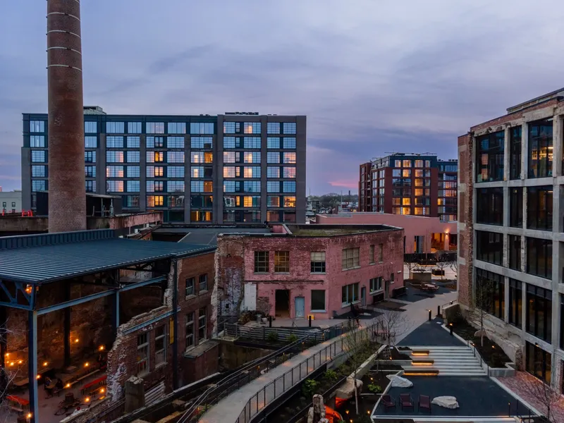Grid-pattern facade of residential tower rising above red brick warehouse buildings at twilight
