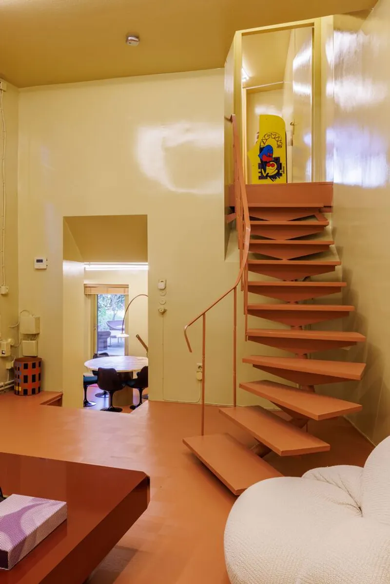 Open tread staircase with orange steel structure and handrail connecting split-level living spaces