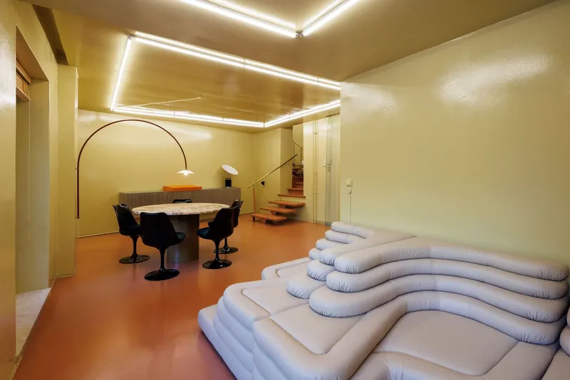 Interior with orange resin floor, recessed ceiling light panel, curved lounge seating, and dining area beyond