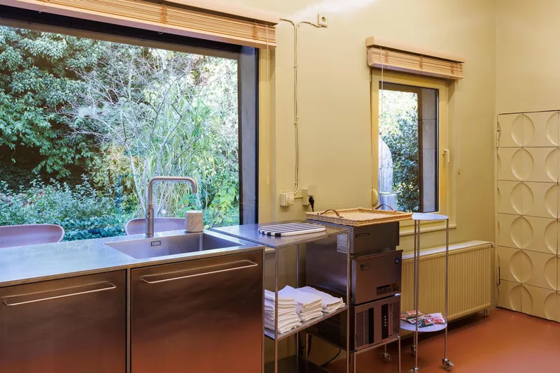 Kitchen with stainless steel counter, window overlooking green garden, and orange resin floor