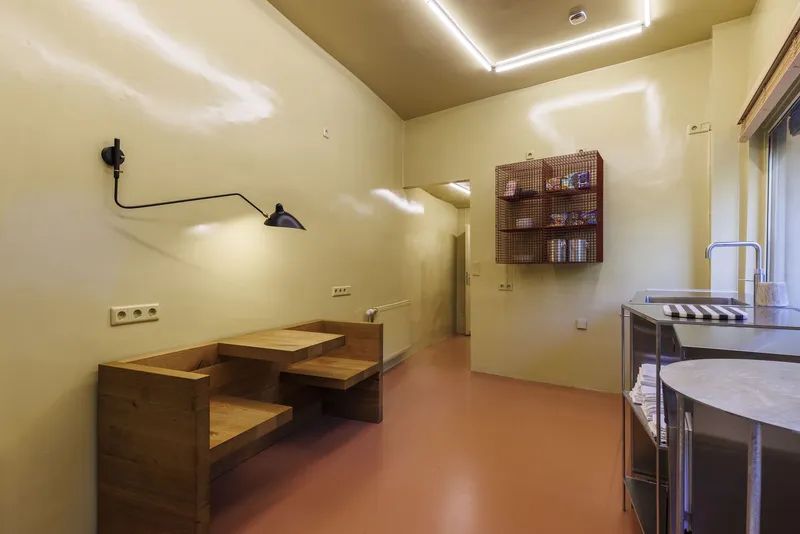 Dining nook with built-in timber banquette, articulated wall lamp, and perforated storage box