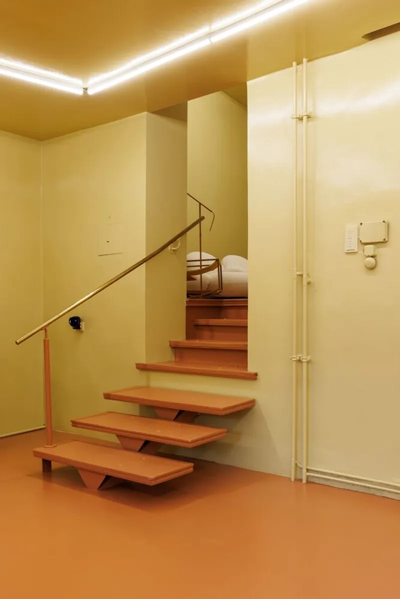 Cantilevered timber stair with brass handrail ascending through cream walls and recessed ceiling cove lighting