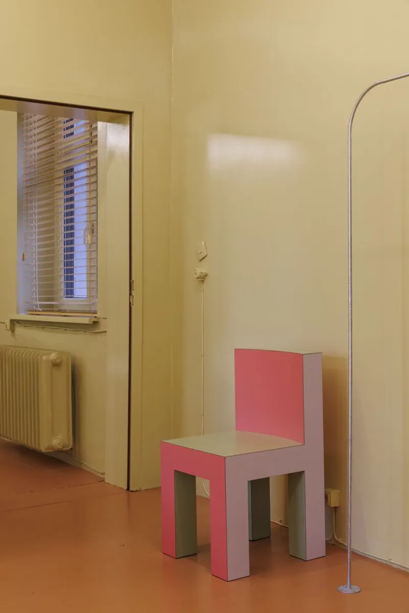 Pink cubist chair against pale yellow walls with orange floor and arched floor lamp