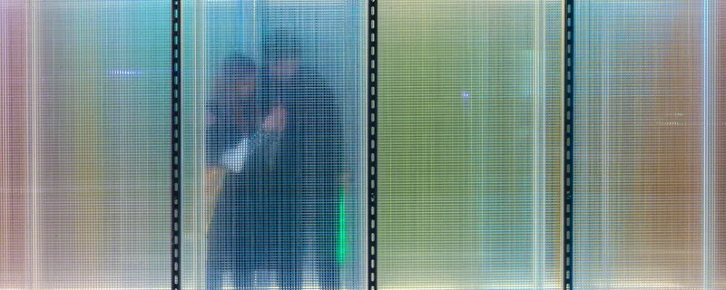 Close-up of translucent corrugated panels in gradient colors with a blurred figure standing behind the surface