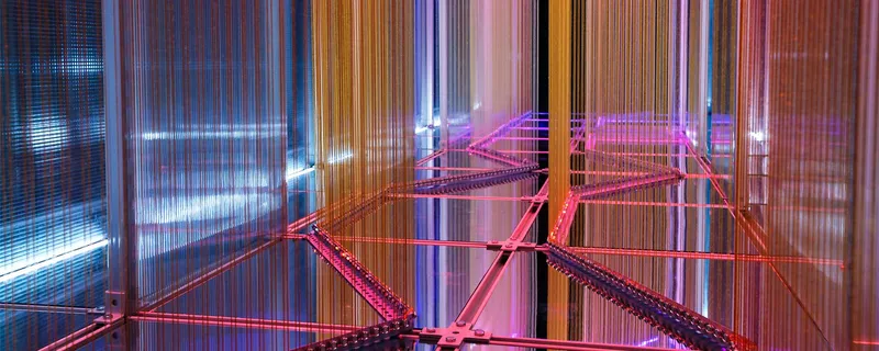 Pink bicycle frames suspended behind translucent polycarbonate panels illuminated by colored light