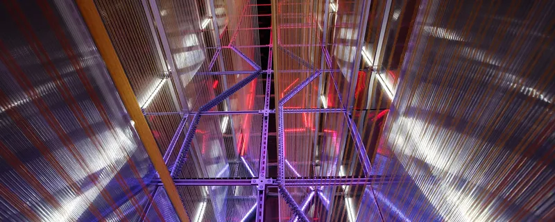Looking up at the steel truss ceiling with purple and pink lighting behind ribbed panels