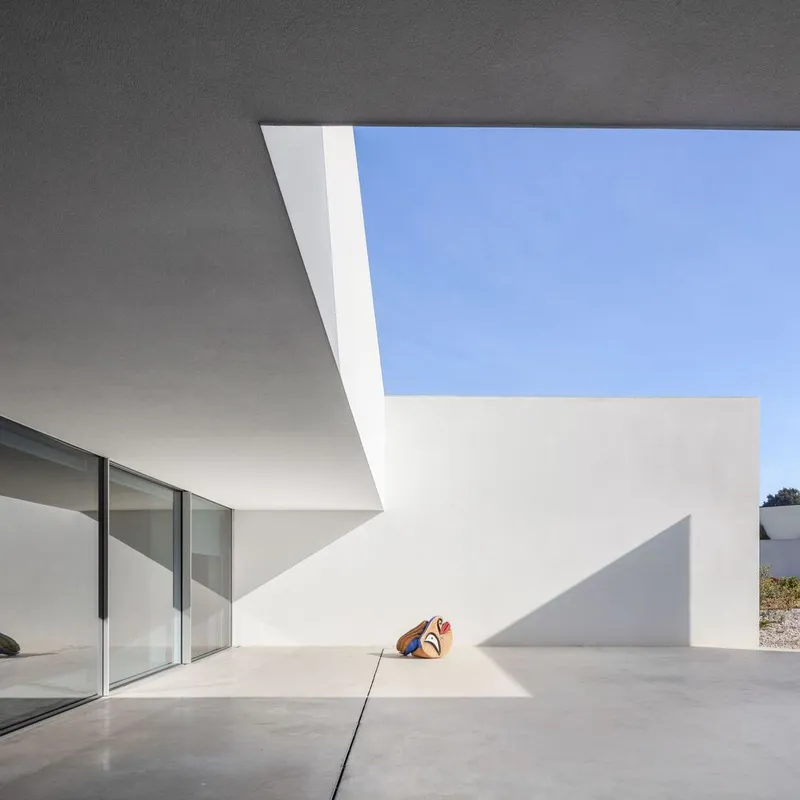 Concrete patio beneath a white cantilevered overhang with sliding glass doors and sharp shadows