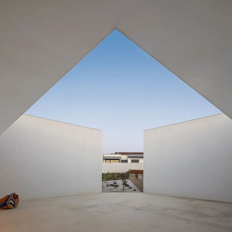 Covered exterior terrace with triangular open roof framing another white building volume beyond