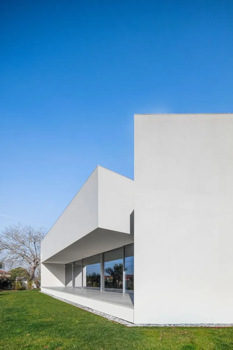 White stucco facade with cantilevered volume sheltering a glazed recessed entry facing a grass lawn