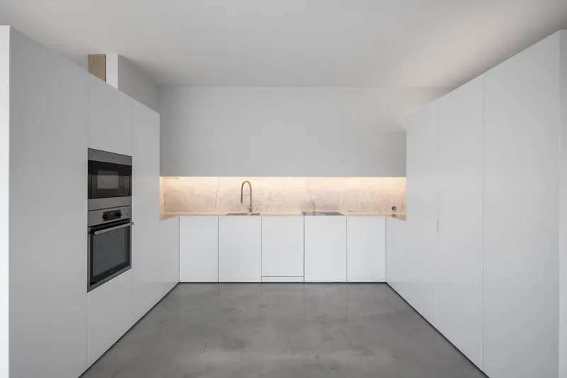White minimalist kitchen with illuminated stone backsplash and grey polished concrete flooring