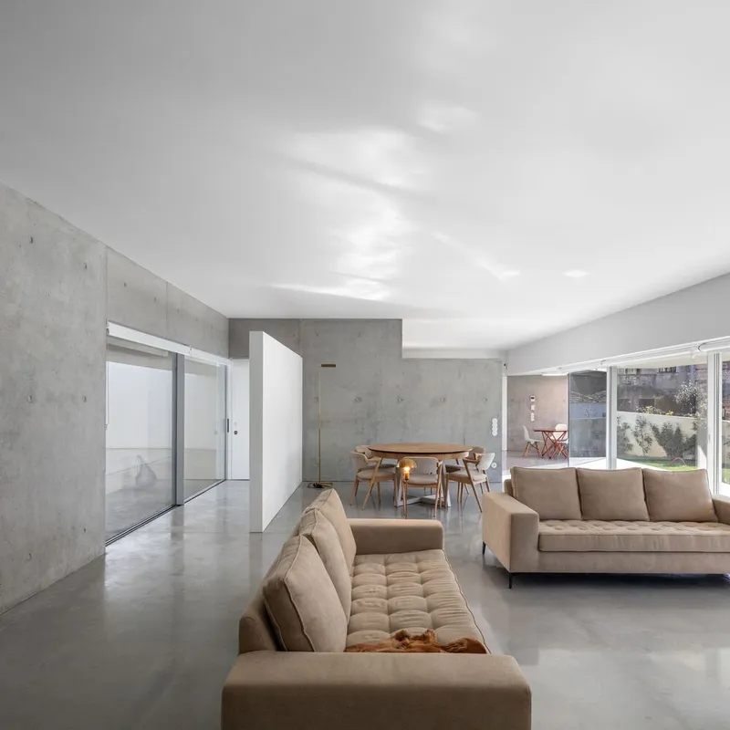 Living area with board-formed concrete walls and tan sofas beneath white vaulted ceiling