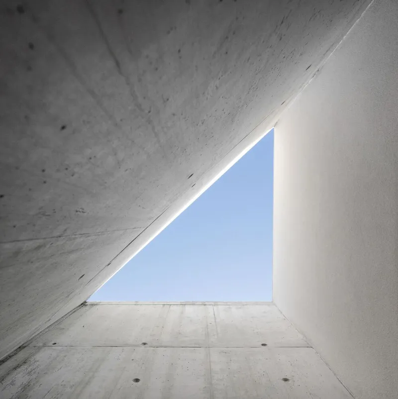 Looking up at triangular skylight framed by concrete walls and white plaster surfaces
