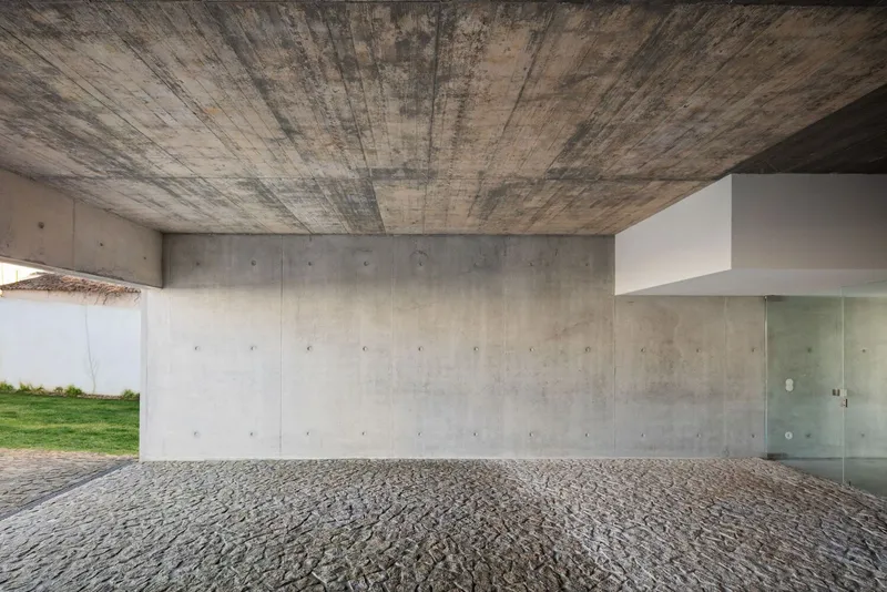 Covered carport with board-formed concrete ceiling and walls over a grey gravel floor