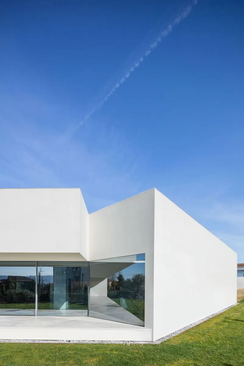 White geometric volumes forming a cantilevered entry terrace against a blue sky with contrail