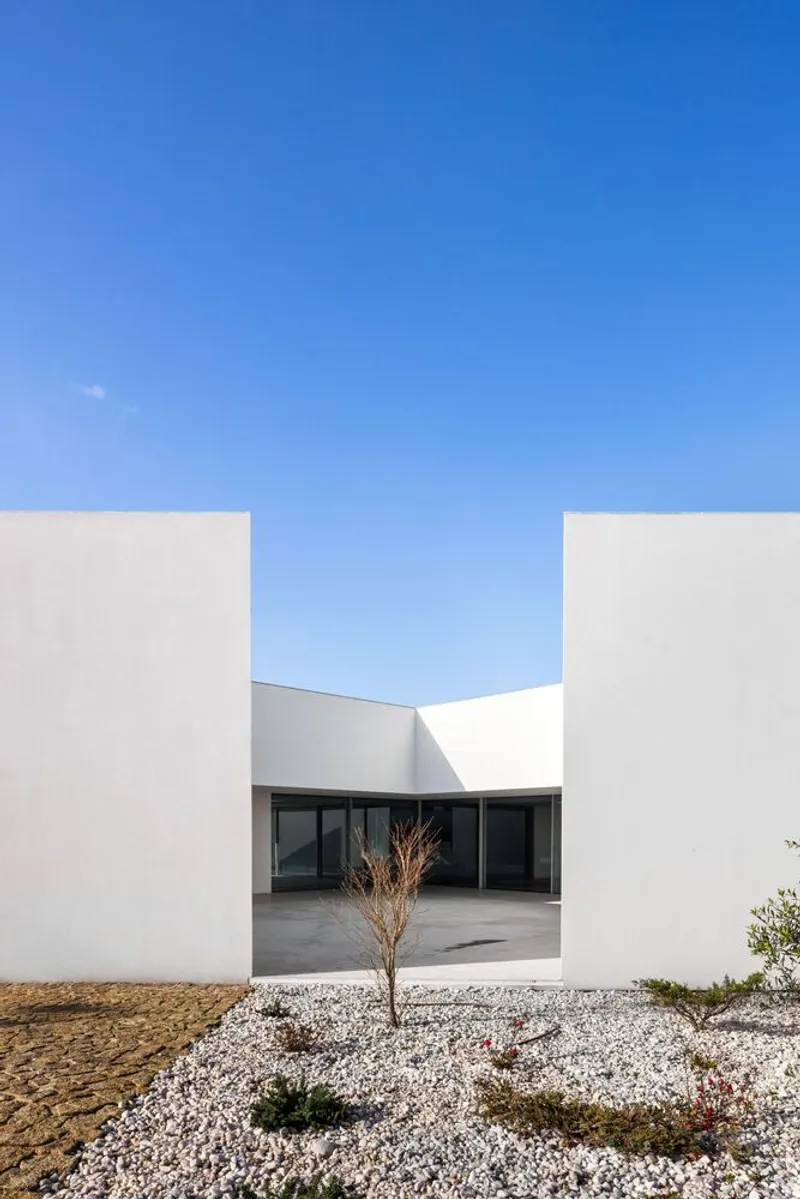 Entry courtyard framed by white stucco volumes with white gravel beds and sparse plantings