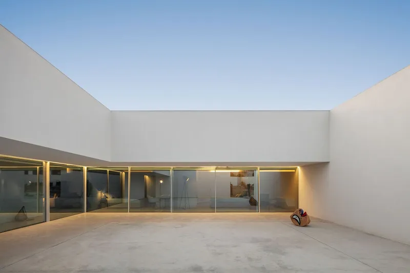 Private courtyard with continuous glass wall and integrated lighting at dusk