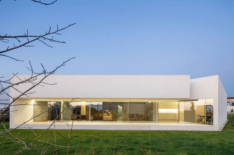 Garden facade with floor-to-ceiling glass below white volumes framed by bare winter branches