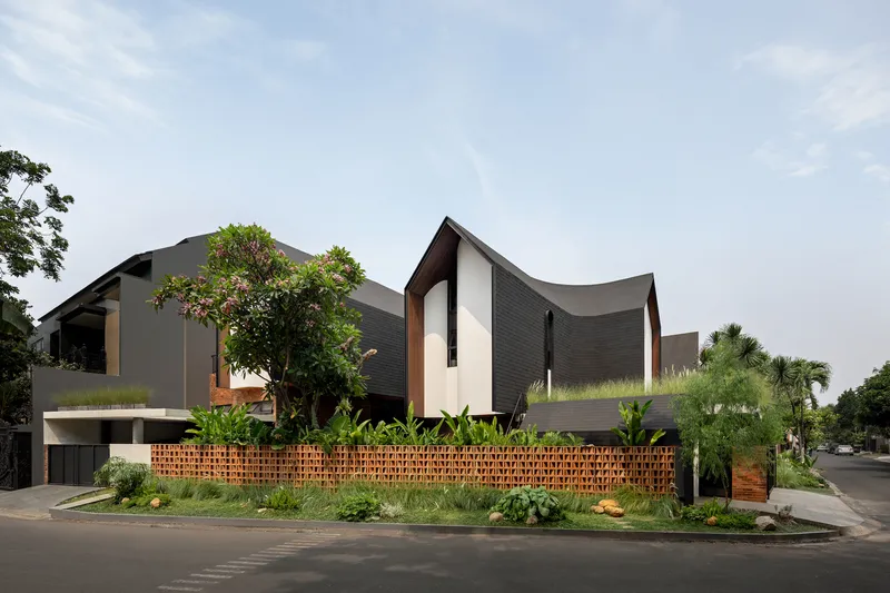Street view of the sculptural roofline with perforated brick fence and planted beds along the sidewalk