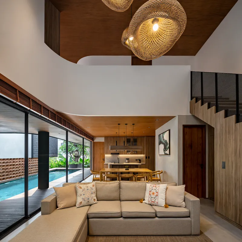 Double-height living room with timber ceiling, woven pendant lights and pool view through sliding glass doors