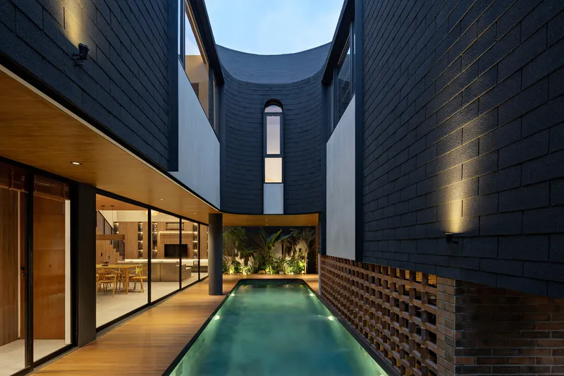 Courtyard pool flanked by dark brick walls and perforated screen at dusk with uplighting