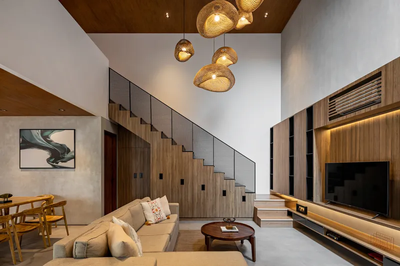 Living room with woven pendant fixtures and timber staircase integrated into storage wall below double-height void
