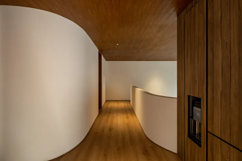 Curved corridor with white plaster walls, timber ceiling and wooden cabinetry under ambient lighting