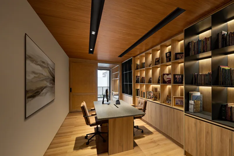 Home office with illuminated timber shelving and desk facing a window with distant figure