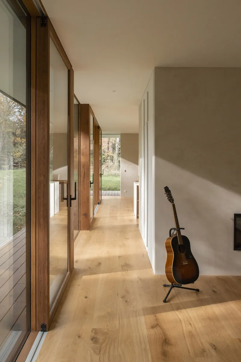 Corridor with timber-framed glazing overlooking autumn landscape and oak flooring with acoustic guitar on stand
