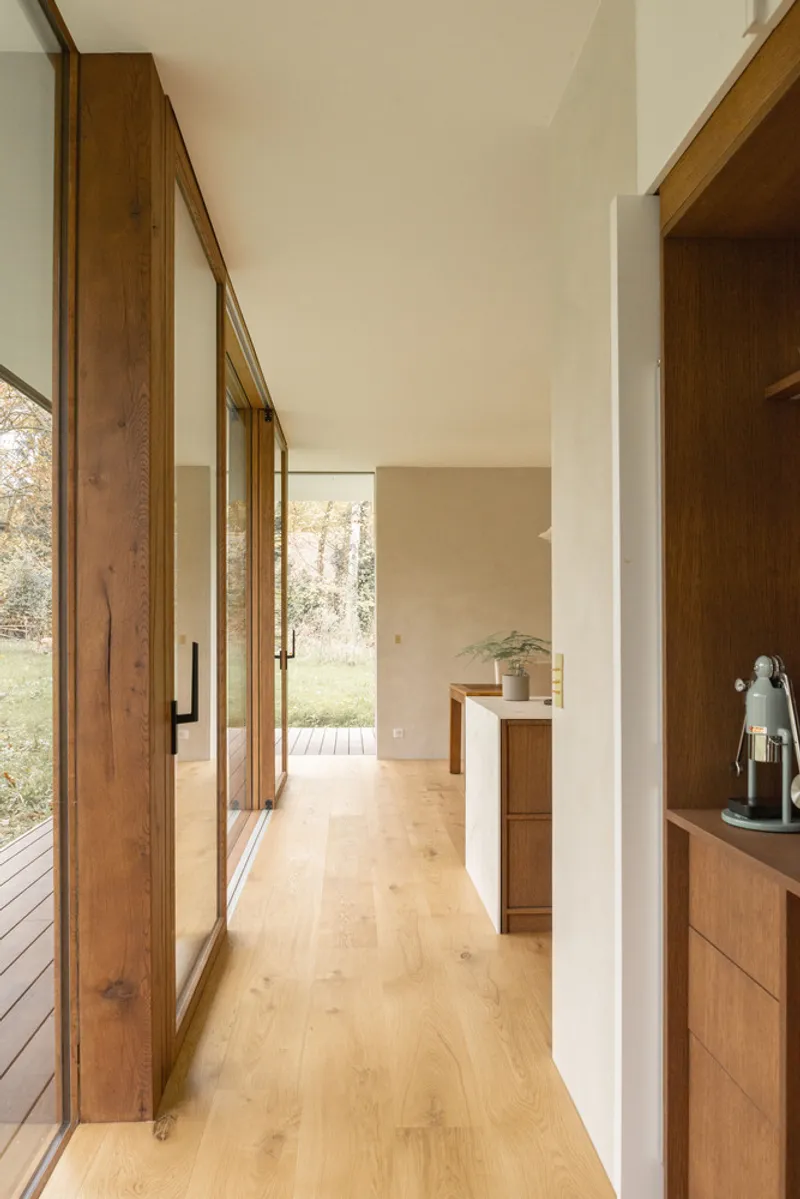 Corridor with timber cabinetry alcove and glazed wall framing view of bare trees and grass